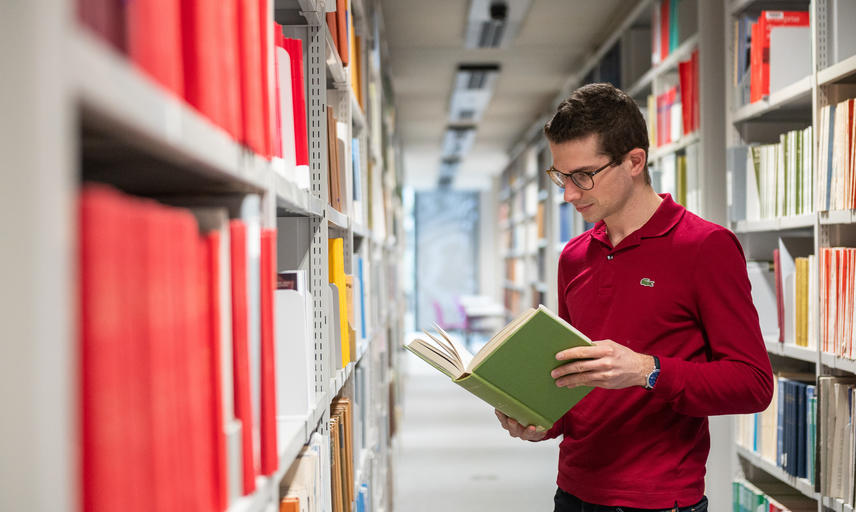 student looks at book in library